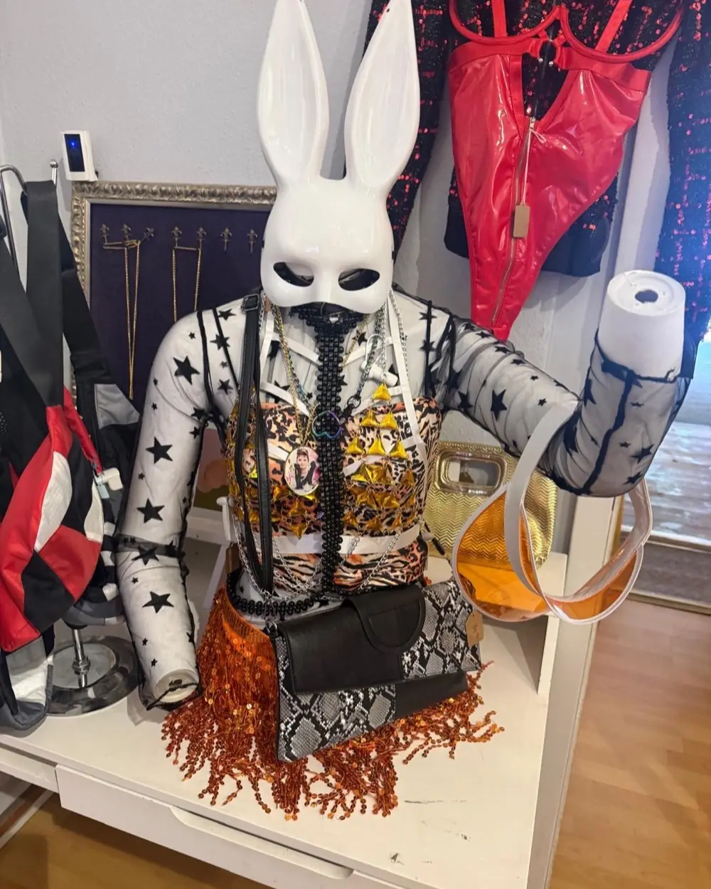 Büste mit weißer Hasenmaske, Leo-Top, Goldschmuck und orangem Paillettenrock